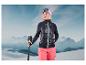 Une femme en tenue de ski avec une veste noire, un pantalon rose et des bâtons de ski dans un environnement montagneux enneigé.
