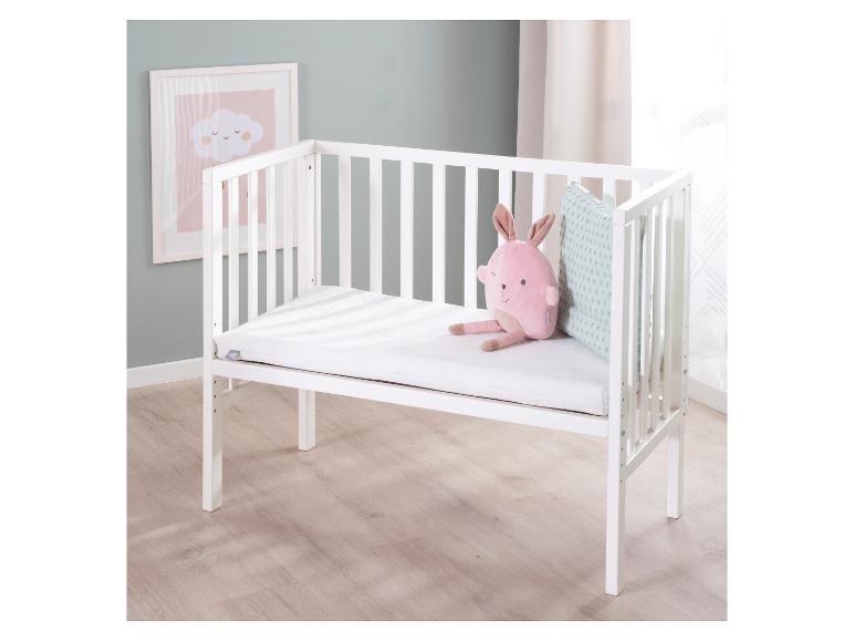 Lit bébé blanc avec une peluche rose et un oreiller, à côté d'un tableau de nuages.