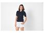 Femme en polo côtelé bleu marine et short blanc, souriant à la caméra.