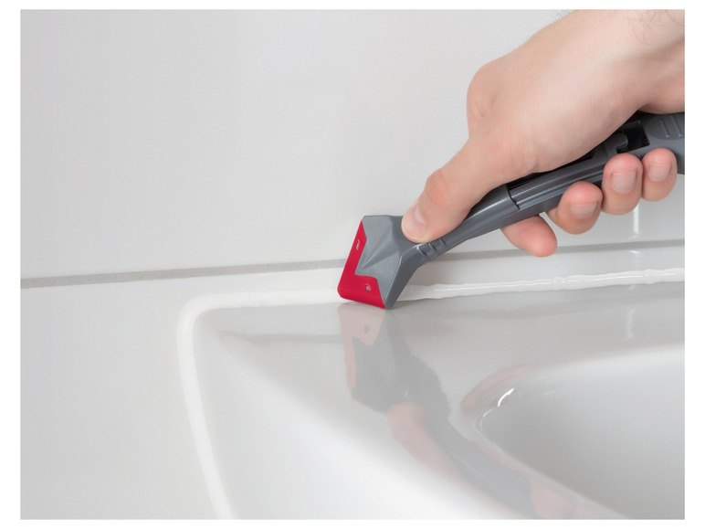 Une main utilisant une spatule pour appliquer du mastic silicone entre des carreaux.