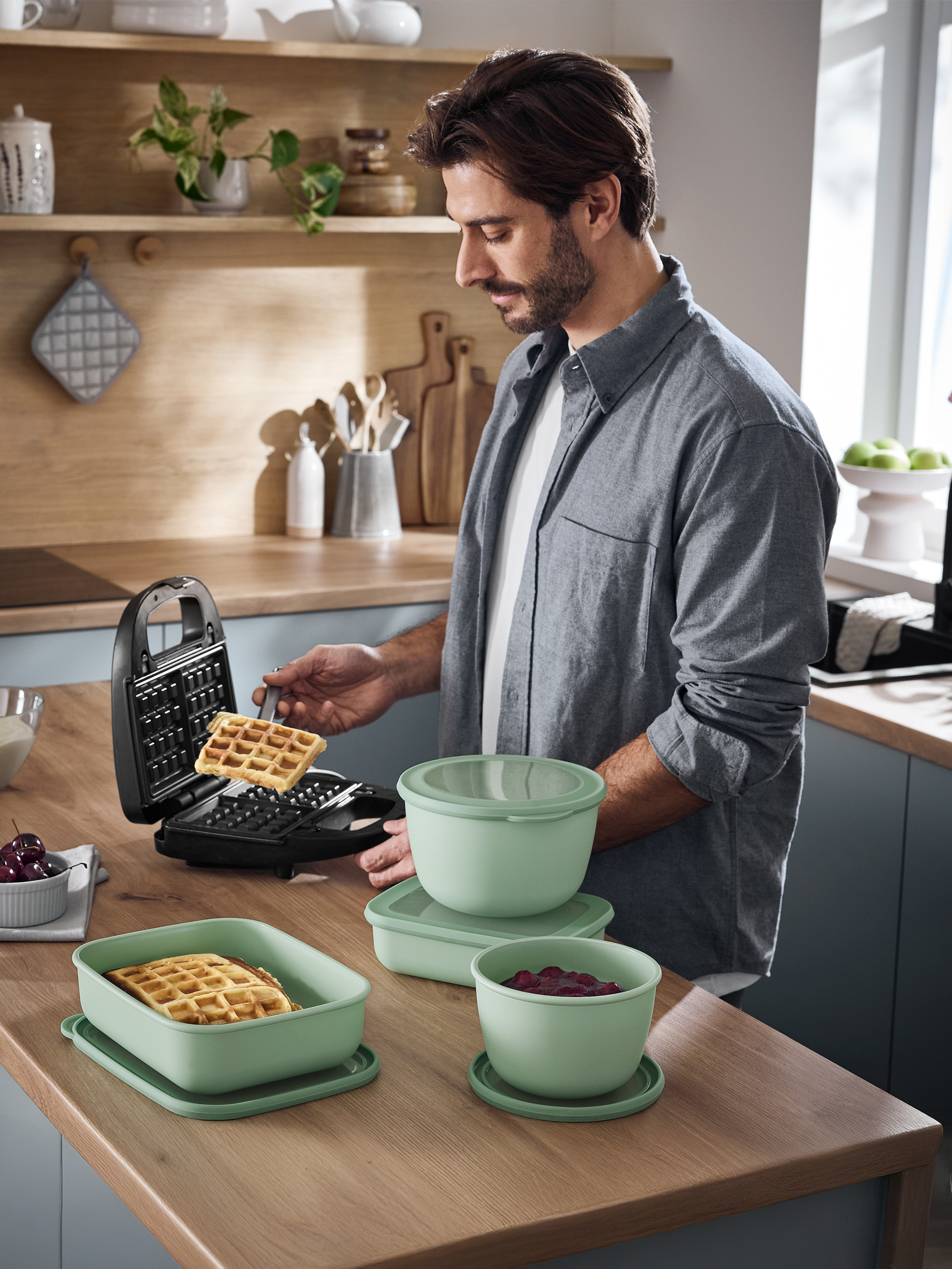 Homme préparant des gaufres avec un gaufrier et les servant dans des récipients verts.