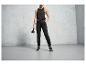 Une femme en pantalon de survêtement noir, un débardeur et des baskets tient un kettlebell.