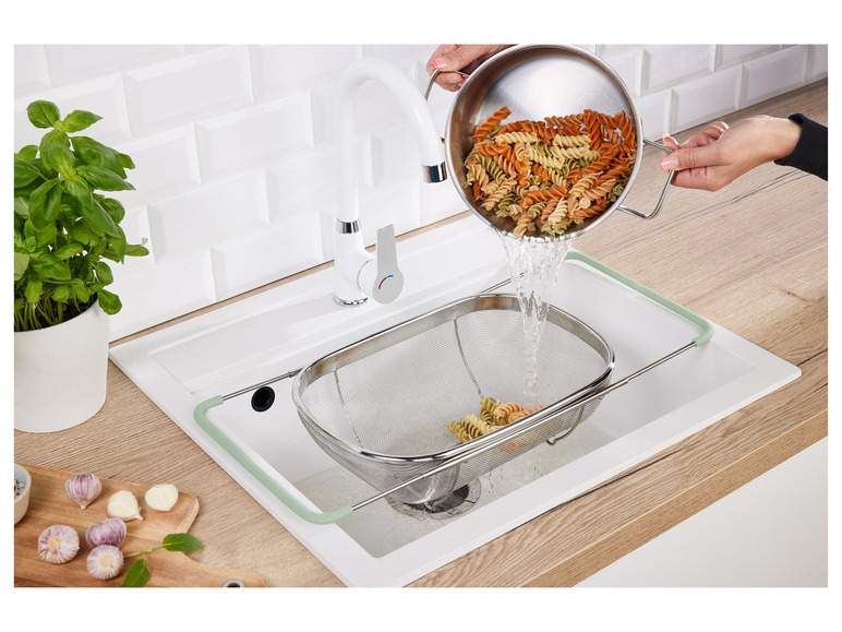 Des pâtes sont rincées dans un évier avec une passoire.