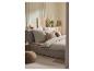 Chambre à coucher avec un lit, une literie claire, des oreillers décoratifs et un pouf tressé.