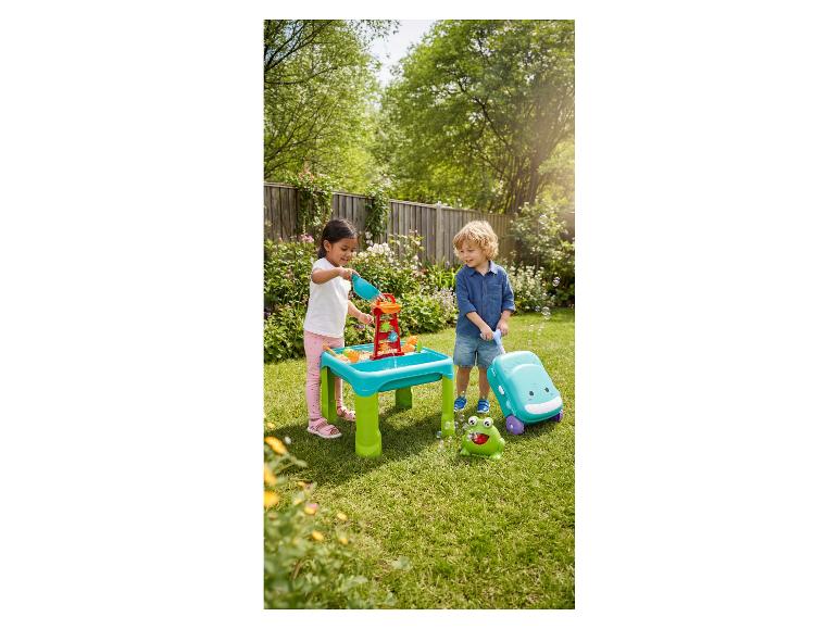 Enfants jouant avec une table d'eau et de sable et des jouets à bulles dans un jardin.