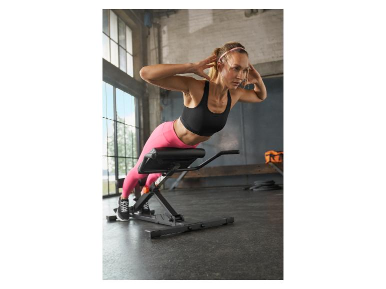 Femme sur un banc d'hyperextension faisant un exercice de dos dans une salle de sport.