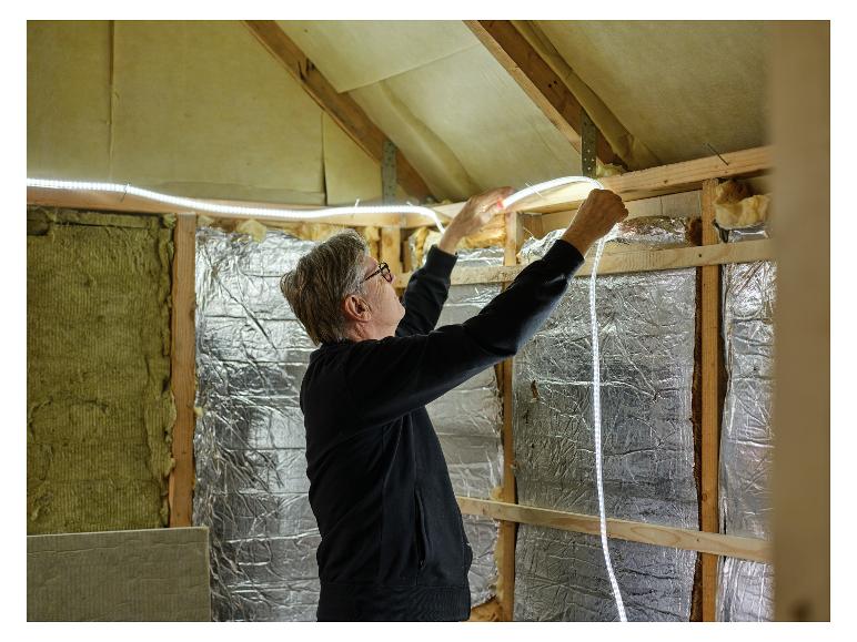 Homme installant le tube lumineux LIVARNO® Leuchtschlauch »The Renovator« dans le grenier.