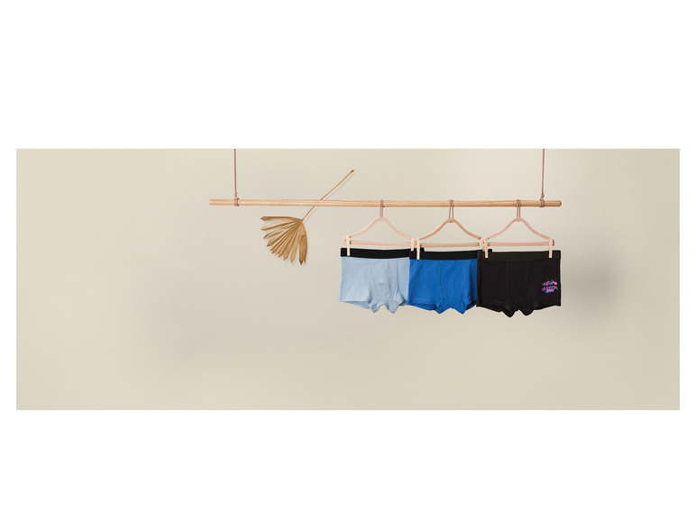 Trois boxershorts, en bleu clair, bleu foncé et noir, sont suspendus à une barre en bois.