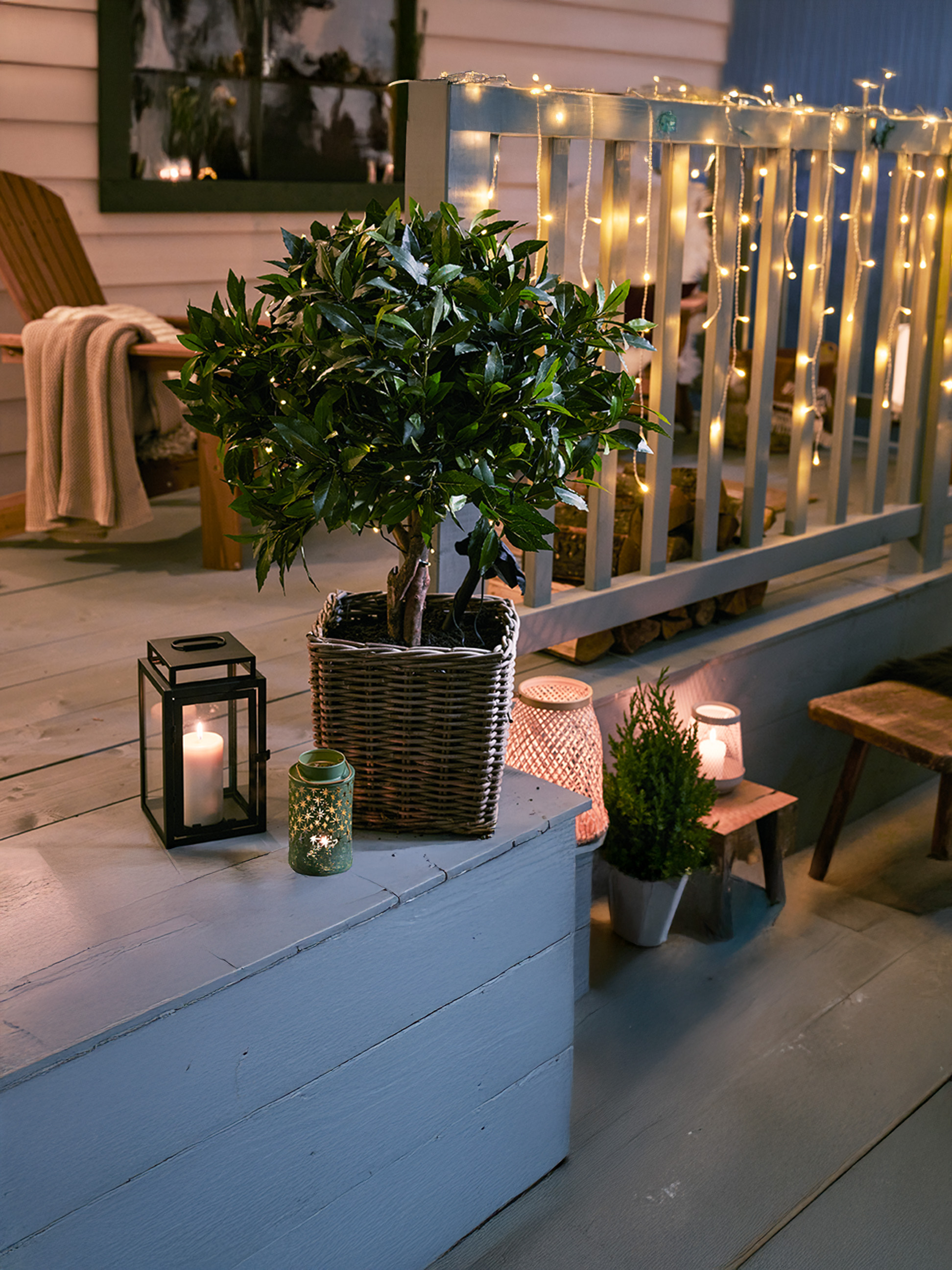 Un patio extérieur confortable la nuit, décoré de guirlandes lumineuses, de lanternes et de plantes en pot.