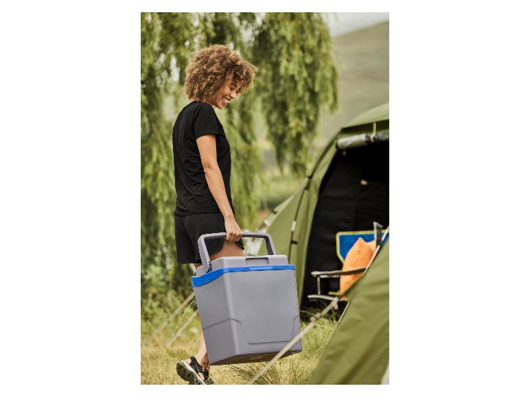 Femme souriante portant une glacière de camping grise à côté d'une tente.