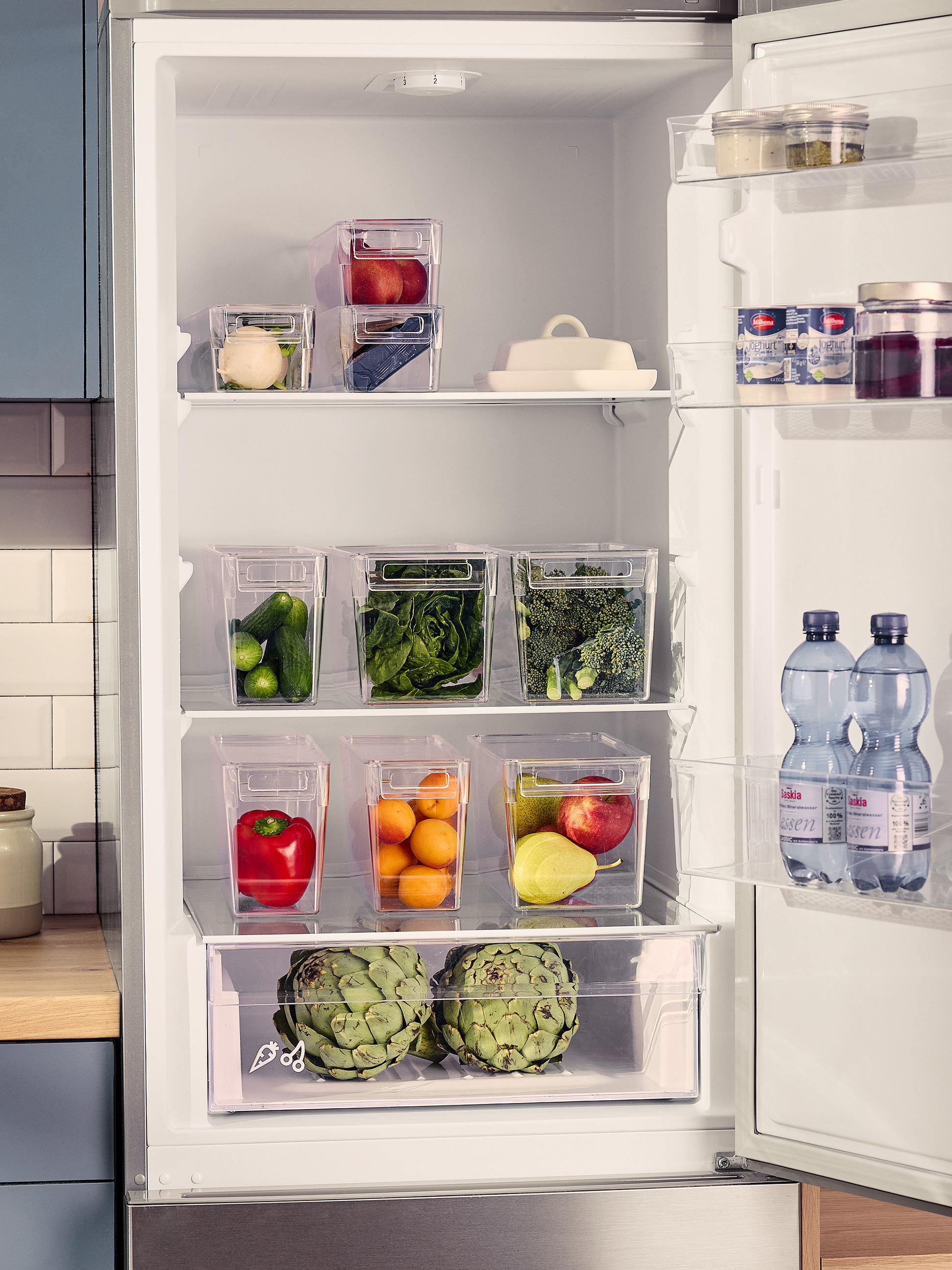 Réfrigérateur ouvert avec des contenants transparents remplis de légumes et fruits frais.
