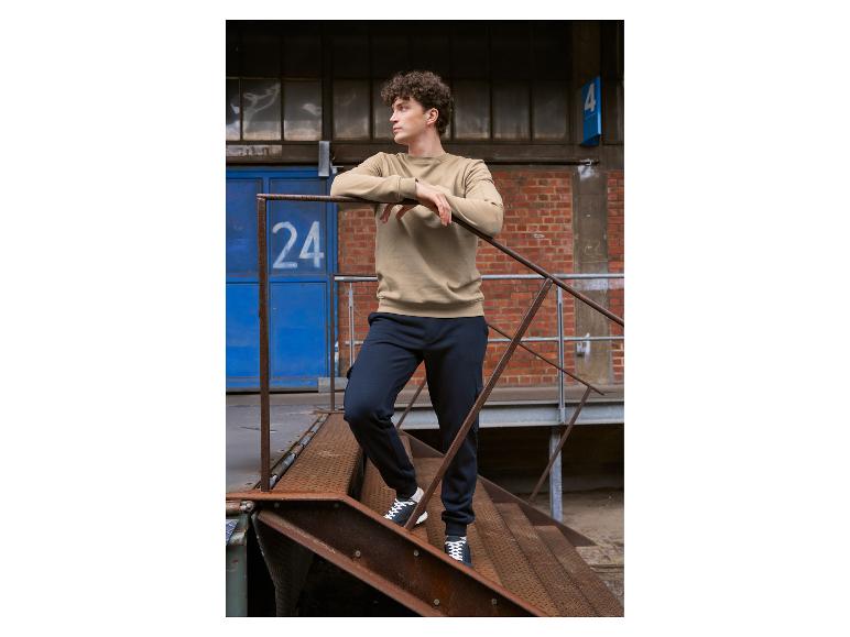 Homme en sweat-shirt beige et jogging bleu marine sur des escaliers industriels rouillés