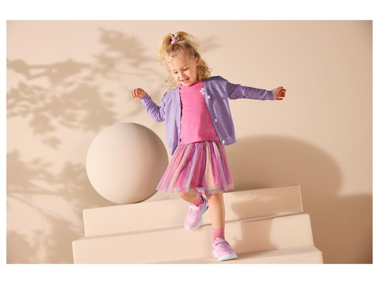 Fille en t-shirt rose, cardigan violet et jupe colorée descendant les escaliers.