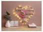 Un porte-photos en métal en forme de cœur avec des lumières, décoré de cœurs en papier rose et de cartes.