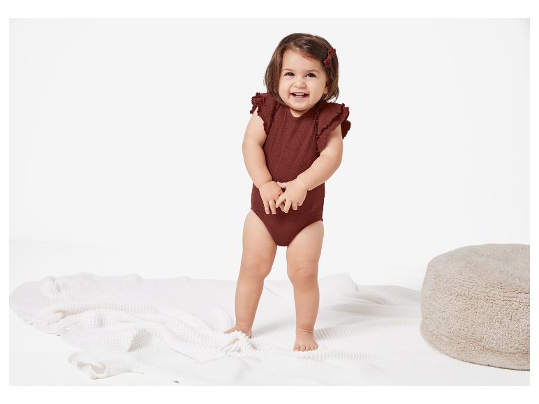 Bébé portant un body marron et une couverture blanche.