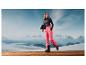 Une femme portant un pantalon de ski rose, des chaussures de ski noires et un casque devant un paysage montagneux.