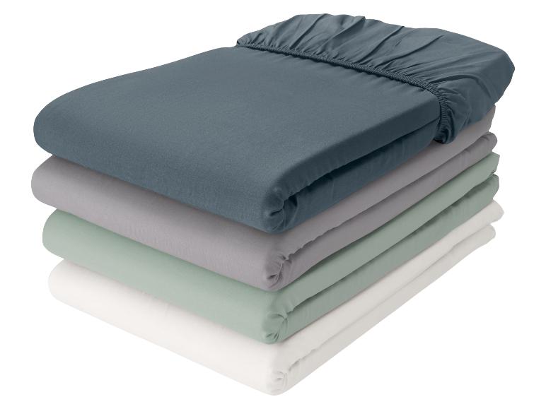 Quatre draps-housses pliés empilés, en bleu, gris, vert et blanc.
