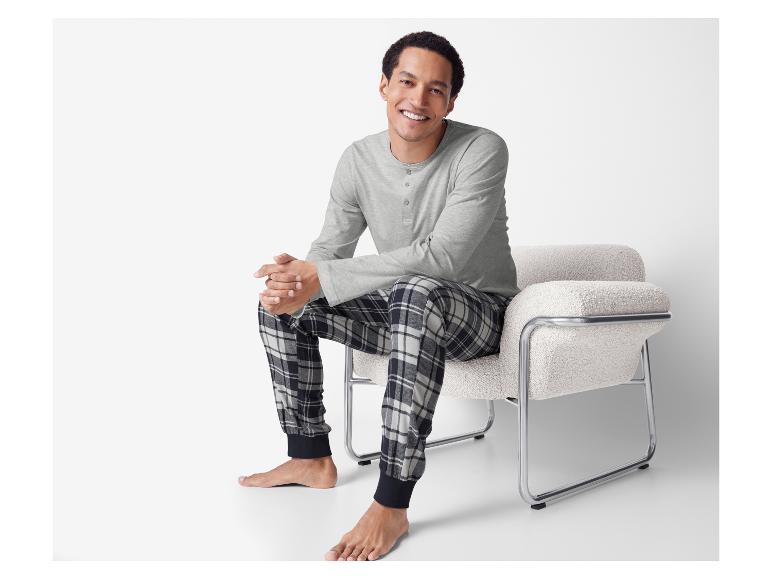 Homme souriant en pyjama à carreaux, assis sur un fauteuil blanc.