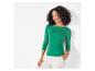 Une femme porte un t-shirt vert à manches trois quarts et un pantalon blanc.