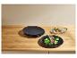 Assiettes noires avec côtelettes d'agneau et légumes, et une assiette avec du pain et des herbes sur une table en bois.
