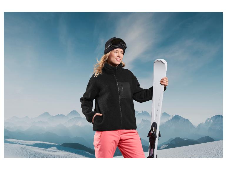 Une femme avec une veste en polaire noire et des skis dans un paysage d'hiver