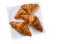 Trois croissants dorés sur une serviette blanche, vue de dessus.