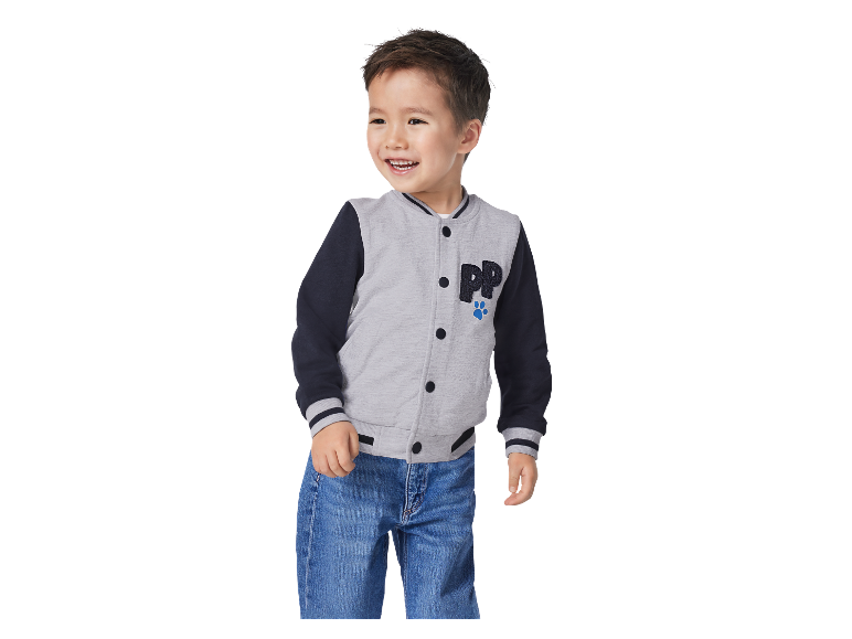 Un jeune garçon souriant porte une veste de baseball gris et bleu marine de Pat' Patrouille.