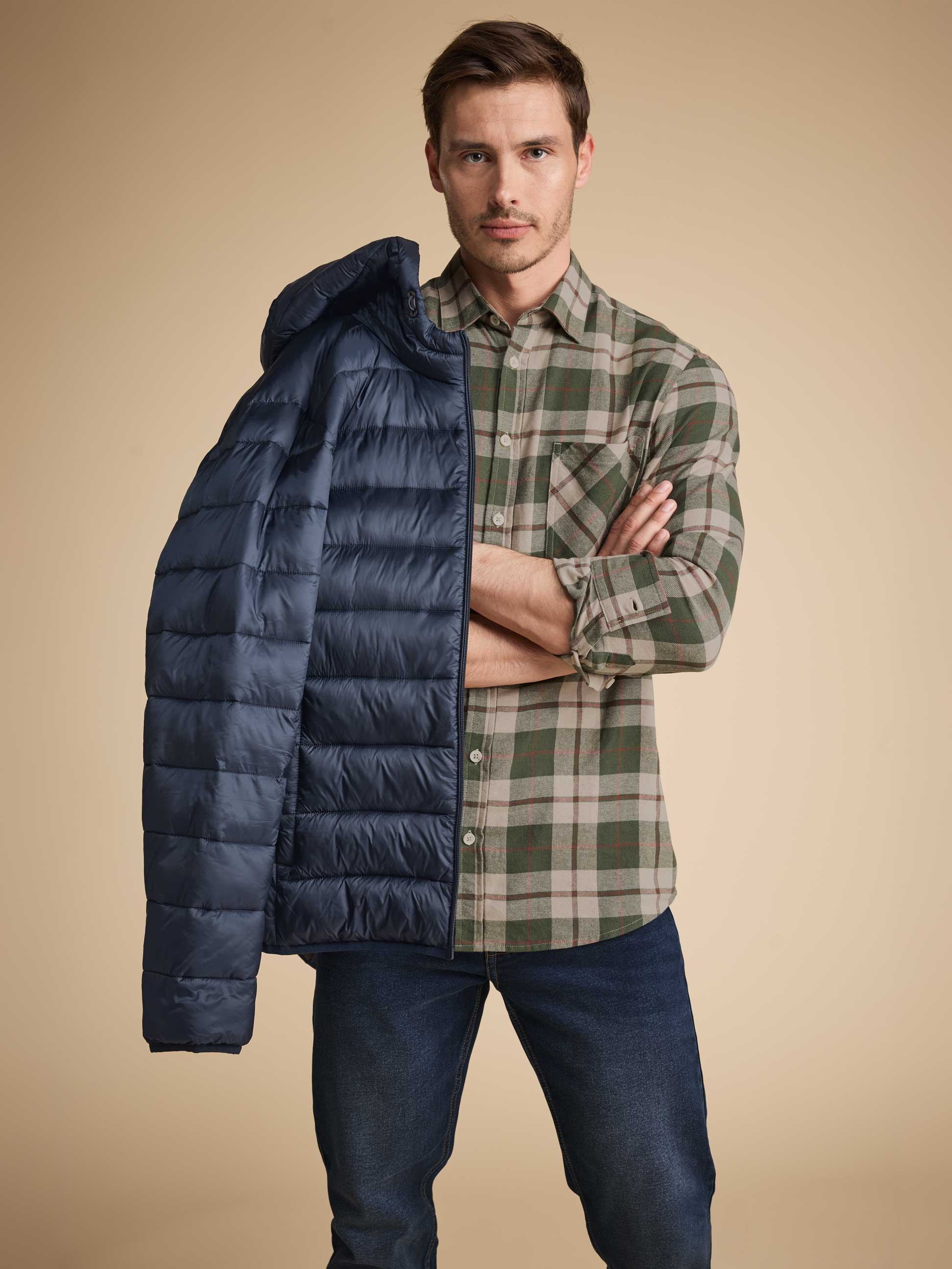 Homme en chemise à carreaux verte et jean, tenant une doudoune bleue sur son épaule.