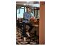 Homme en chemise bleue et baskets blanches assis sur un tabouret de bar dans un café.