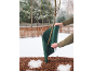 Personne enveloppant un rosier avec une protection hivernale verte dans un jardin enneigé.