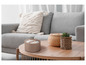 Une bougie parfumée ou décorative allumée sur une table basse avec un panier et une plante.