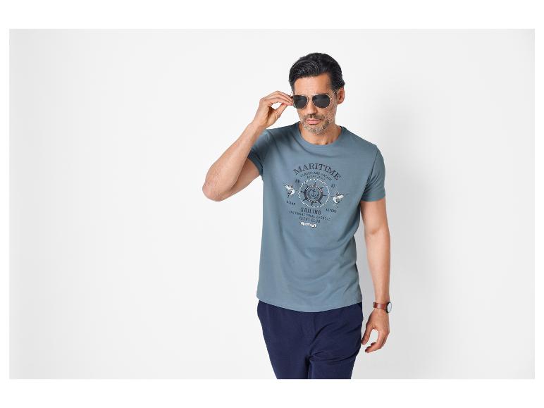 Homme en t-shirt bleu à imprimé maritime, pantalon bleu foncé et lunettes de soleil.