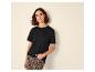 Femme en T-shirt noir et pantalon léopard, appuyée contre un mur.