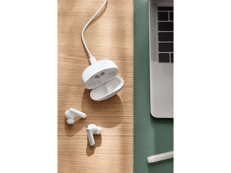 Écouteurs sans fil blancs avec boîtier de charge sur un bureau en bois à côté d'un ordinateur portable