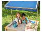 Deux enfants jouant dans un bac à sable avec un parasol bleu.