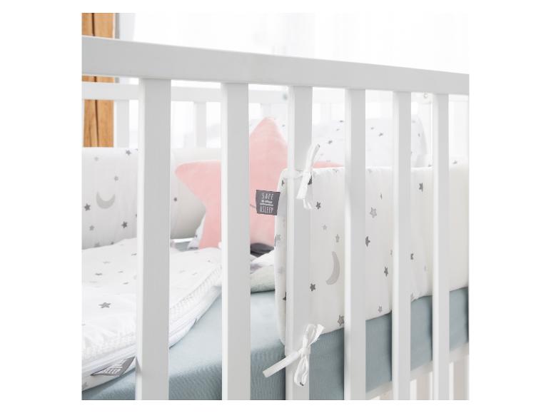 Lit de bébé avec literie blanche à étoiles et lune, et un oreiller rose.