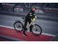 Femme en tenue de cyclisme noire et gants jaunes avec un vélo électrique sur un pont.