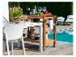 Chariot de service en bois, table et chaises blanches près d'une piscine.