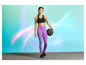 Femme en soutien-gorge de sport noir et leggings violets tenant un ballon de fitness.