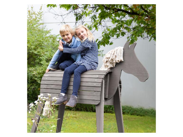 Deux enfants jouent sur un cheval à bascule en bois dans un jardin.