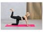 Une femme en leggings noirs et un soutien-gorge de sport fait un exercice sur un tapis de yoga rose.