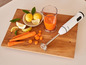 Un mixeur plongeant blanc Silvercrest, du jus d'orange et des carottes sur une planche à découper en bois.
