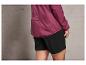 Une femme portant une veste coupe-vent rose avec le mot 'ACTION' et un short noir.