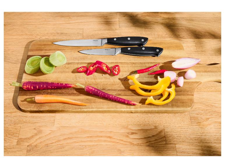 Couteaux de cuisine et légumes frais coupés sur une planche à découper en bois.