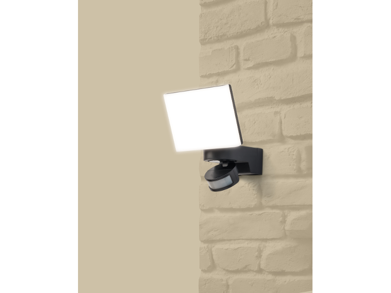 Projecteur LED extérieur avec détecteur de mouvement monté sur un mur en briques.