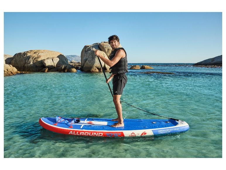 Homme sur paddleboard gonflable bleu et rouge dans une eau claire, avec des rochers en arrière-plan.