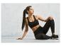 Une femme en soutien-gorge de sport noir et leggings pose sur un fond gris.