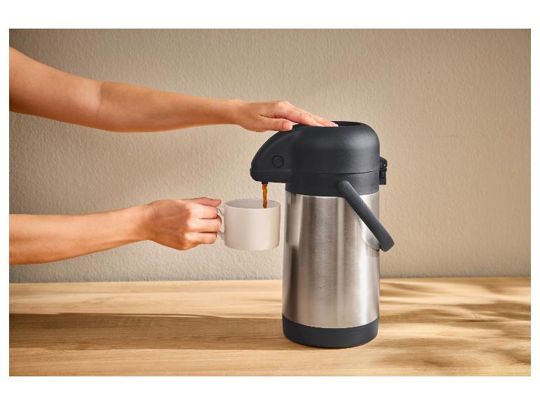 Une personne verse du café d'un thermos argenté dans une tasse blanche.