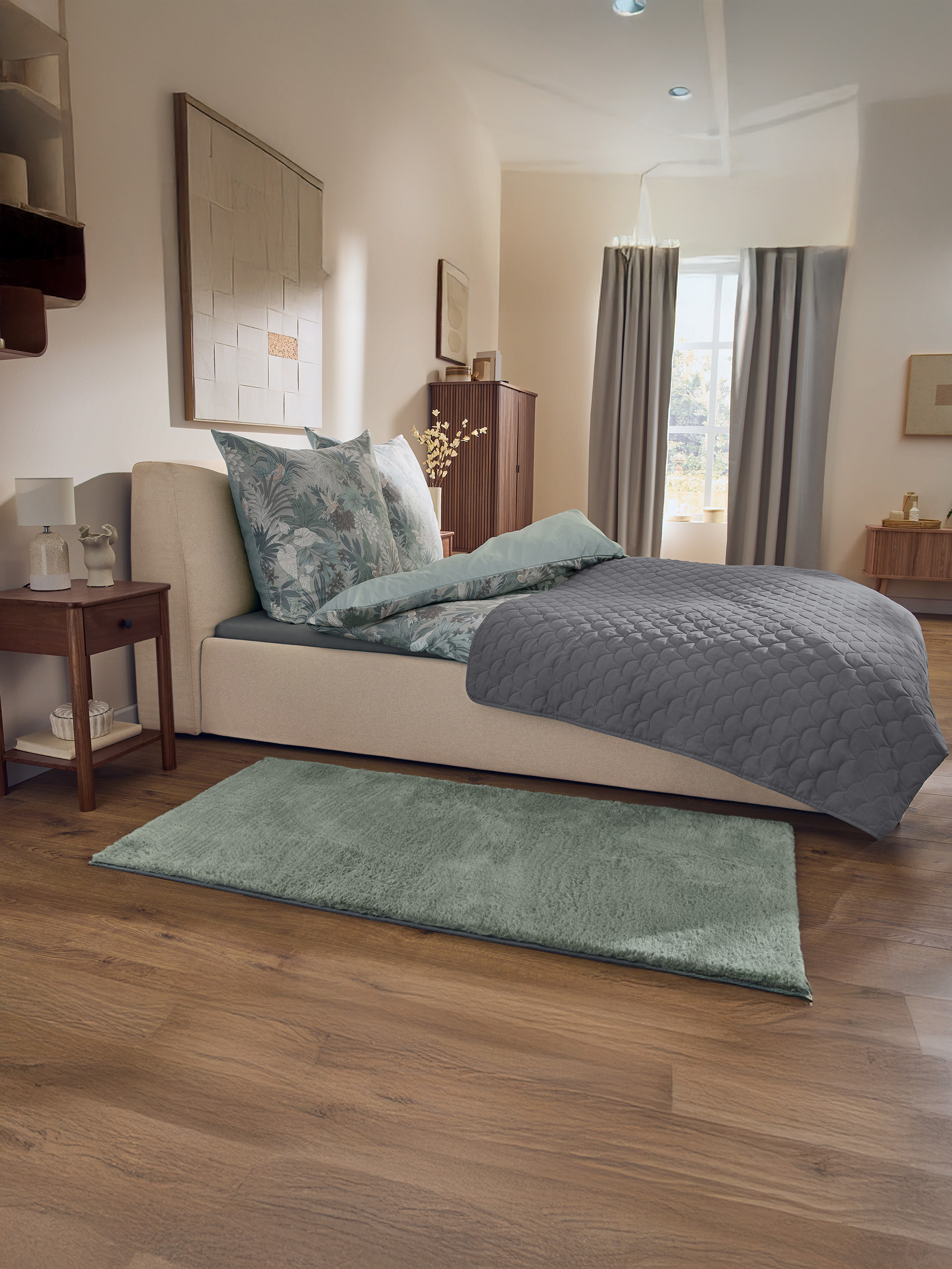 Chambre avec lit beige, parure de lit florale, couvre-lit gris et tapis vert
