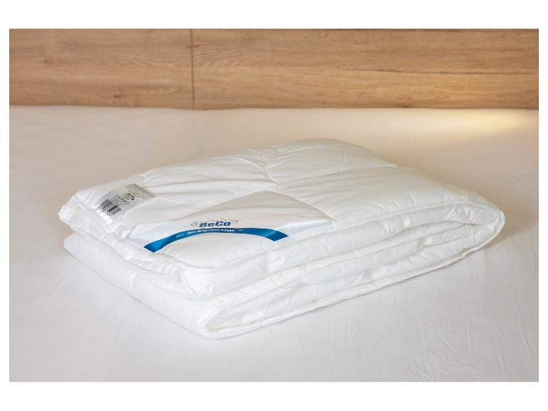 Une couette blanche pliée avec l'étiquette BeCo visible, posée sur un lit.